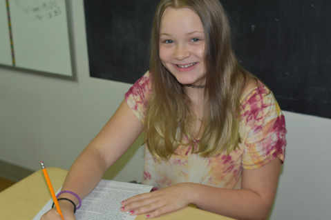 A special euducation student smiles at the camera while working on an assignment