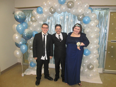 Three special education students smile in formalwear under a balloon arch as they get ready for their prom