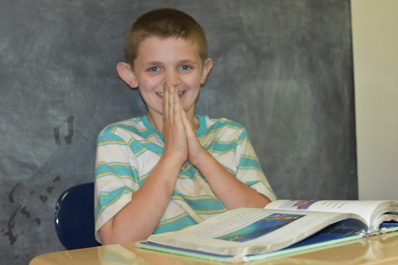 A special euducation student smiles at the camera while working on an assignment