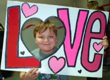 A young boy smiles while posing with a love sign at his special needs school.
