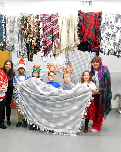 Four elementary special education students and their teacher wear holiday items and pose with a blanket