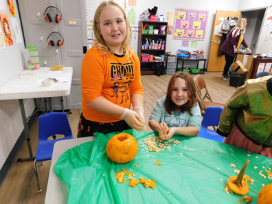 Two young girls smile at the camera while they carve a pumlin at their special education school 