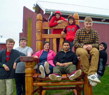 A group of special education students and teachers pose on a giant rocking chair during a pumpkin patch trip
