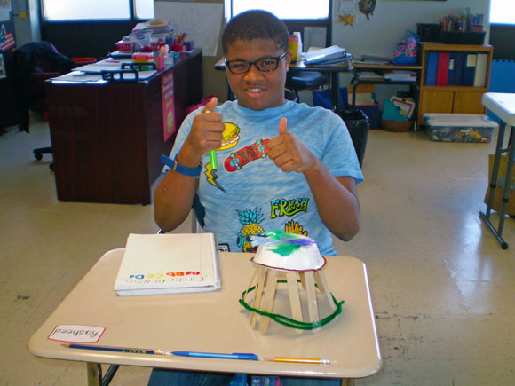 A special education student gives a thumbs up to the camera while showing off a project he is working on