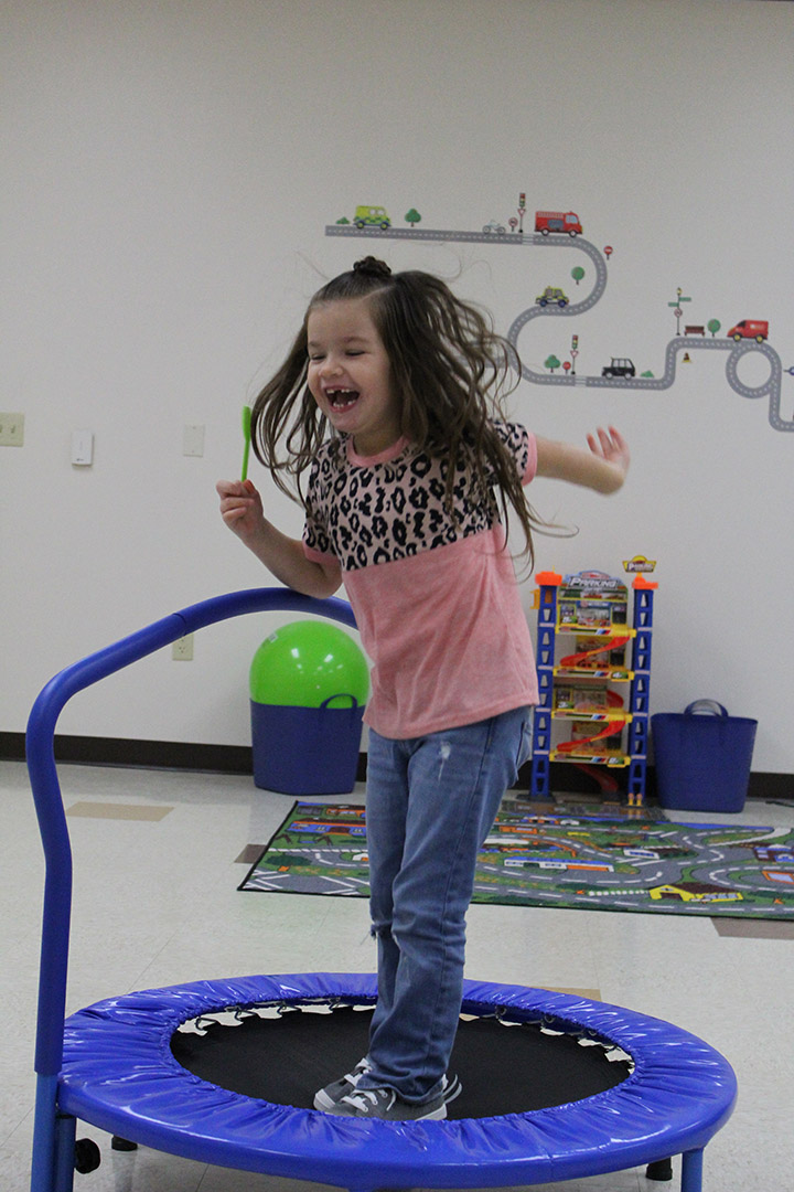 Special Education Student jumping on a trampoline in the natural skills room. She's mid jump, smiling widely, arms flailing.