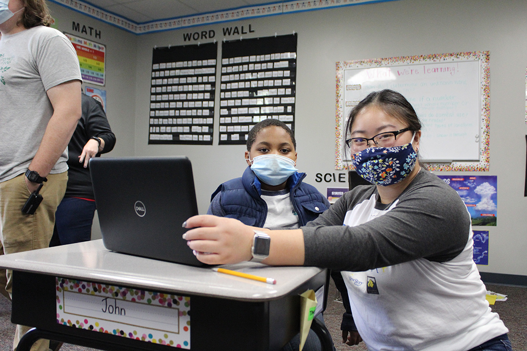 Teacher and Special education student wear masks and work on a laptop at a desk. 