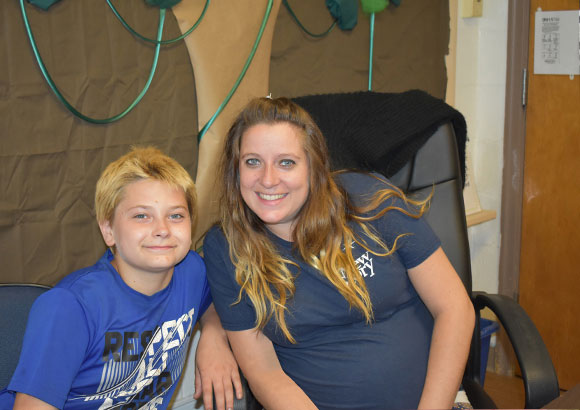 A special education student and teacher smile together in their classroom.
