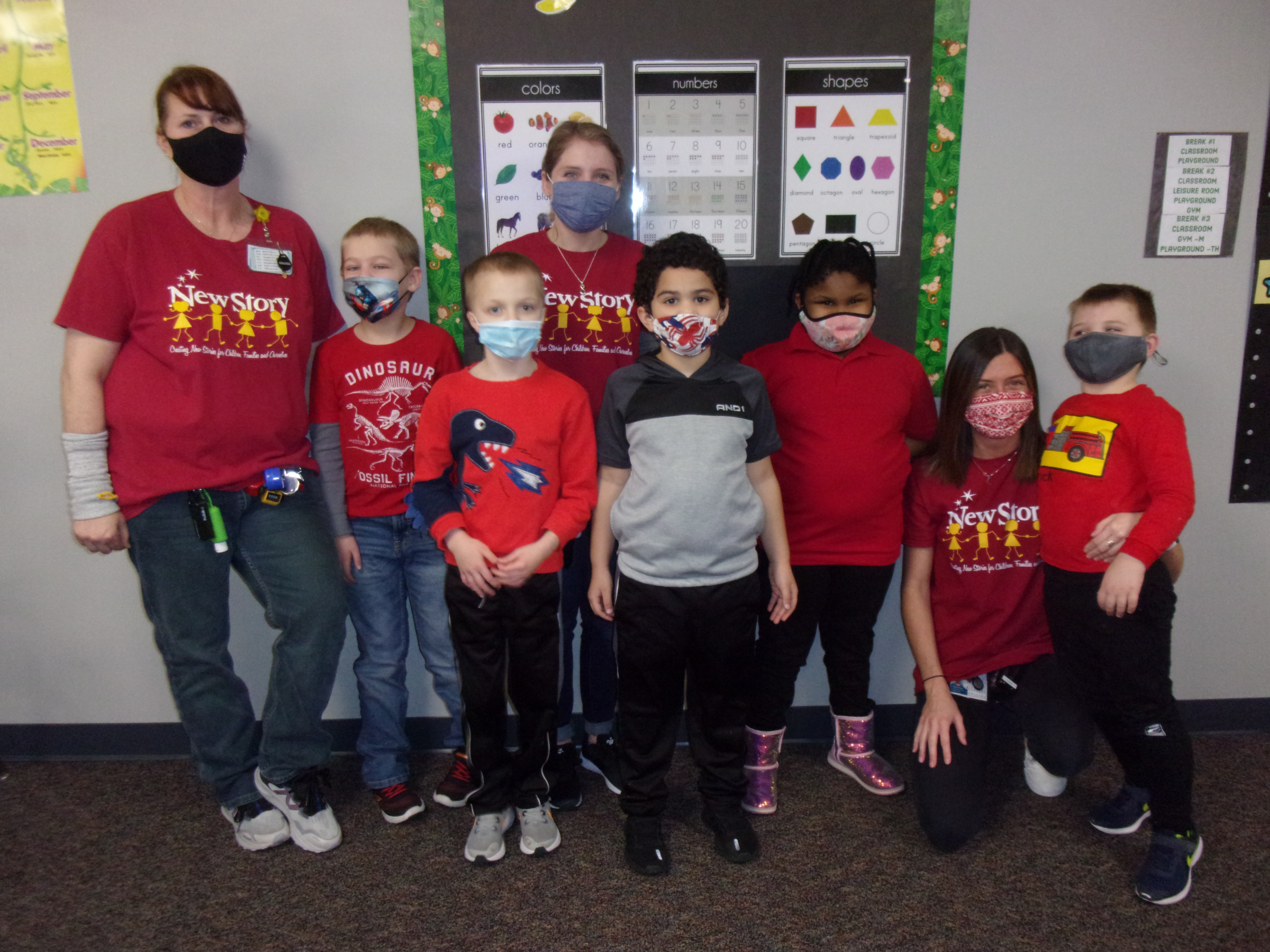 Students and staff dressed in shades of red stand in front of a bulletin board.