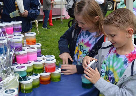 A group of students explore a table full of paints at an outdoor event.