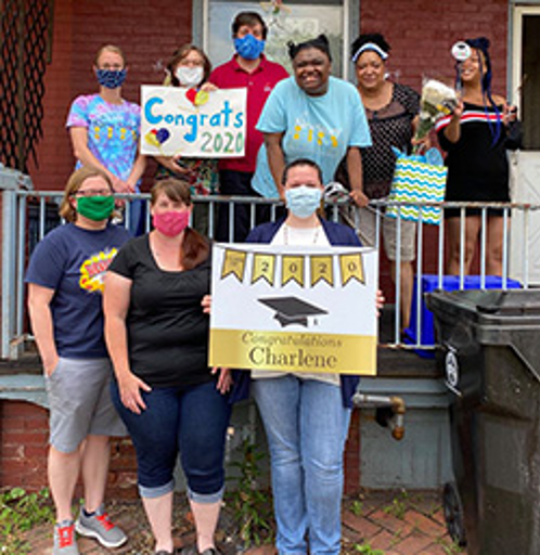 Teachers and staff came to student's home to celebrate. Student is on porch with her family and New Story Staff holding congrats signs. Student has biggest smile!